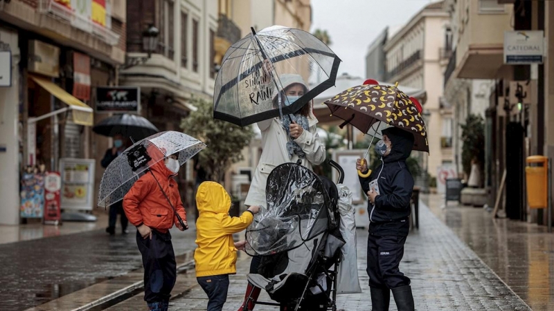 Una mujer con tres menores se protegen de la lluvia con paraguas y chubasqueros en una céntrica calle de València.