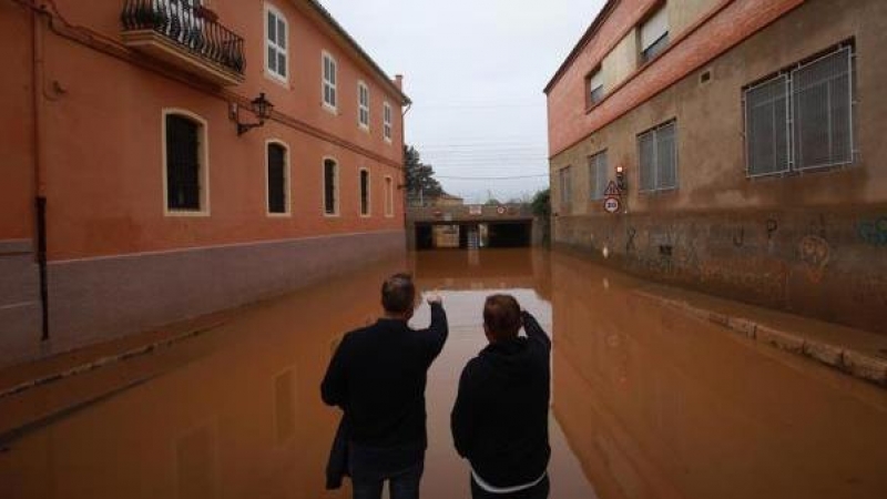 Dos hombres observan el acceso a un paso inferior de la vía ferroviaria inundado por el temporal que afectó en la localidad valenciana de Carcaixent.