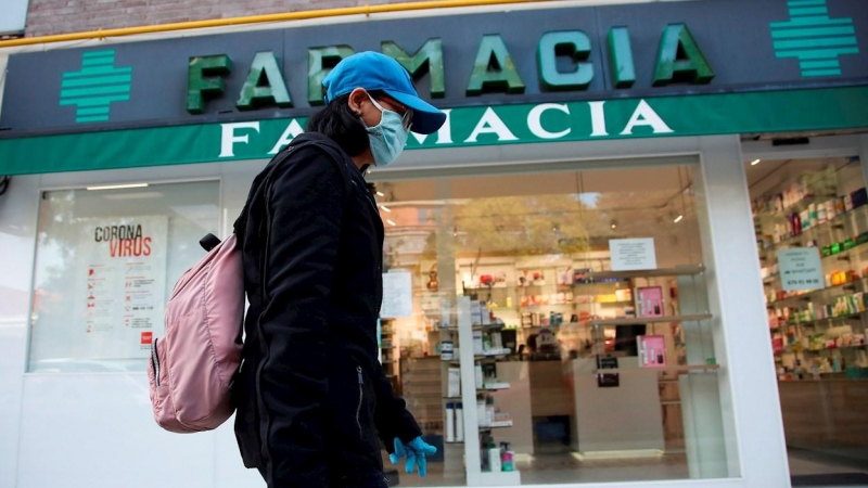 Imagen de archivo de una viandante, protegida con guantes y mascarilla, pasa por delante de una farmacia.