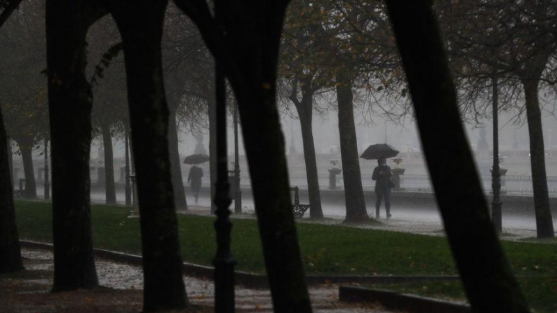 Algunos paseantes se protegen con paraguas de un fuerte chaparrón caído en San Sebastián.