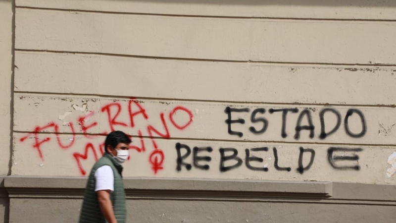 Un hombre camina frente a un muro con pintadas contra la destitución de Martín Vizcarra.