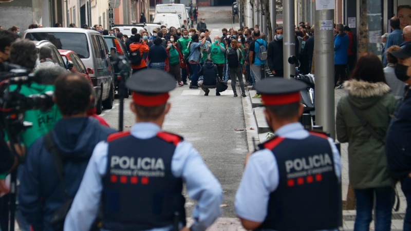 3.	Dos agents dels Mossos d’Esquadra, d’esquena, miren cap als membres de la PAH concentrats per evitar un desnonament previst al carrer Borràs, a Nou Barris, el 4 de noviembre de 2020.