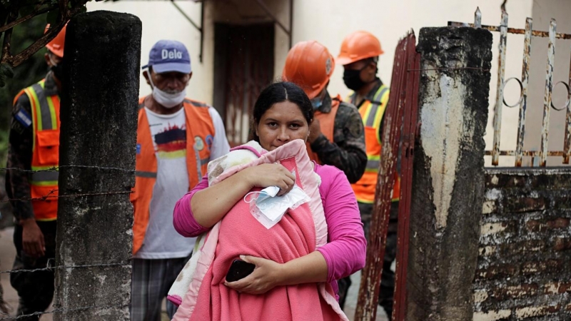 Una mujer que lleva a su hijo sale de su casa mientras los soldados hondureños evacuan a los residentes en previsión de las fuertes lluvias a medida que se acerca el huracán Iota, en Marcovia, Honduras.