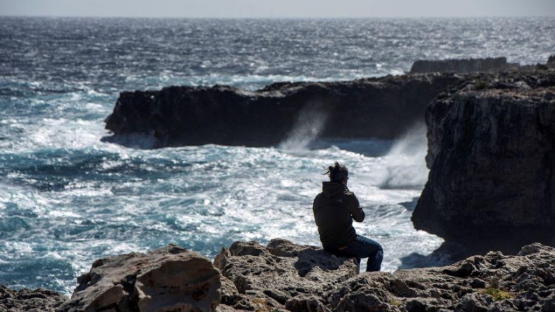 Un joven observa romper las olas en un fuerte oleaje en Menorca.