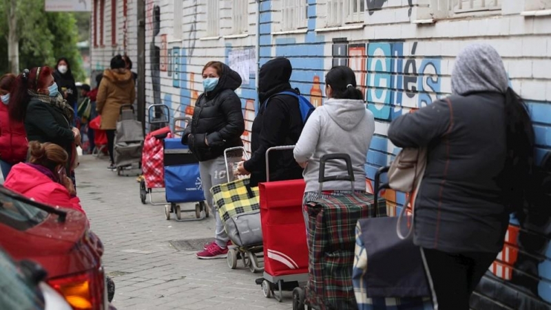 Varias personas esperan en la fila para recoger alimentos proporcionados por la Asociación de vecinos de Aluche. (RODRIGO JIMÉNEZ | EFE)