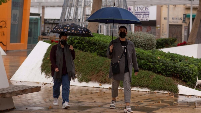 Dos personas se protegen de las lluvia bajo sus paraguas en Málaga.