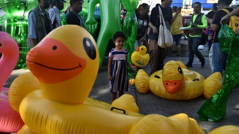 Una niña sostiene un pato inflable de juguete mientras está de pie en medio de versiones más grandes del mismo artículo mientras los manifestantes a favor de la democracia se reúnen.