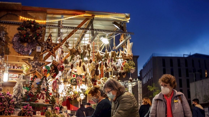 Varias personas junto a un mercadillo navideño este lunes en el centro de Barcelona. EFE/Enric Fontcuberta