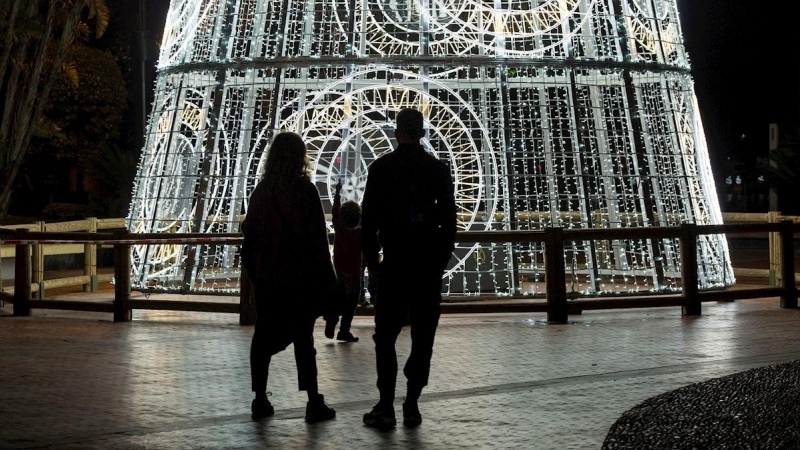 Una pareja y su hijo observan un árbol de navidad iluminado en la Plaza de la Marina, en Málaga.