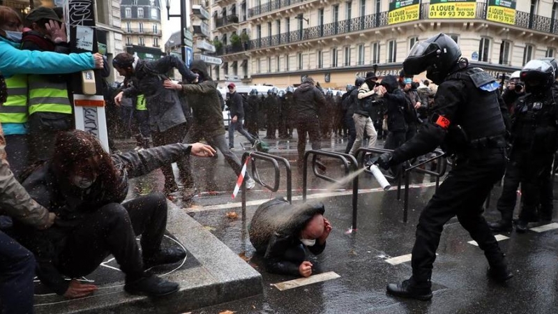 Un agente de policía francés echa spray sobre un manifestante en el suelo.