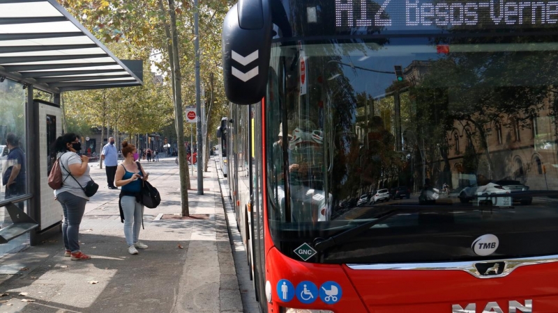 Un bus aturat a la plaça Universitat amb usuaris a la parada.