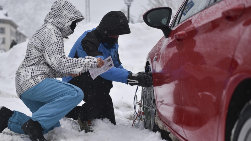 Dos personas ponen las cadenas a las ruedas de su coche por la nieve