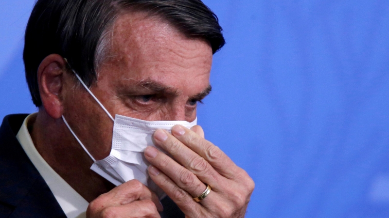 El presidente de Brasil, Jair Bolsonaro, ajustándose la mascarilla.