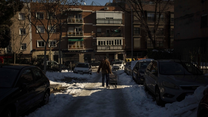 Un hombre carga con el carro de la compra sobre una calle llena de hielo en Carabanchel, Madrid.