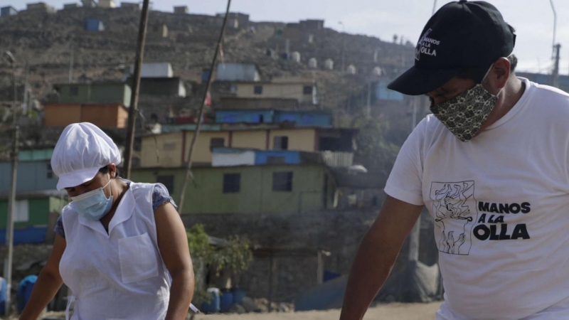 Dos personas cargan una olla en el asentamiento humano de Buena Vista el 2 de febrero de 2021, en el populoso distrito limeño de Villa María del Triunfo, en Lima