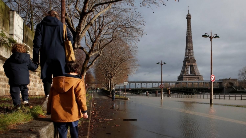Una mujer pasea con sus hijos bordeando el río Sena por su crecida con la torre Eiffel de fondo en París.