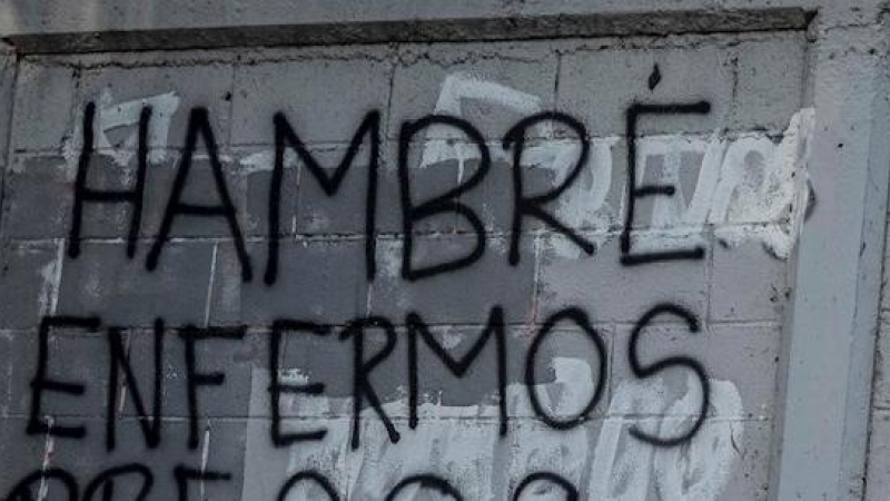 Una mujer camina frente a una pared con un graffiti pintado que dice 'Hambre, enfermos, presos, refugiados' el 8 de febrero de 2021, en Caracas (Venezuela).