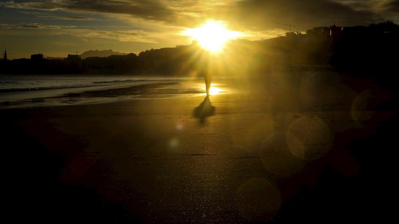 Un hombre observa el amanecer en la playa de Ondarreta de San Sebastián.