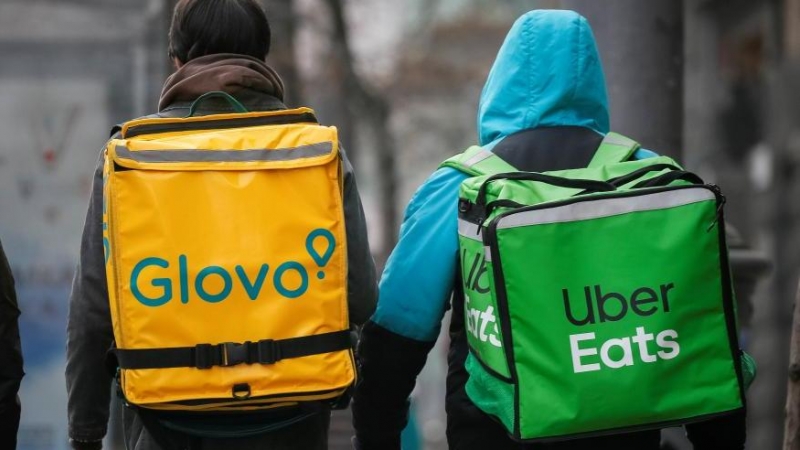 Un 'rider' de Glovo y otro de Uber Eats caminan por una calle principal .Reuters