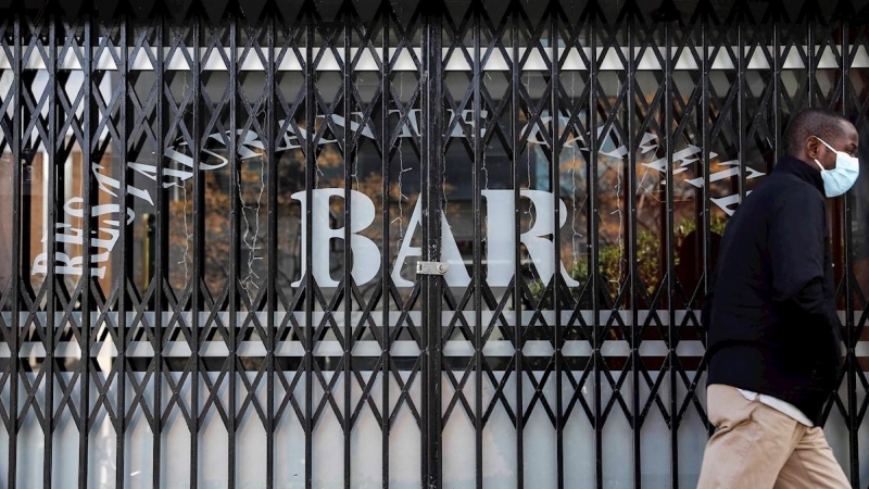 Una persona pasa por delante de un bar que permanece cerrado en València.