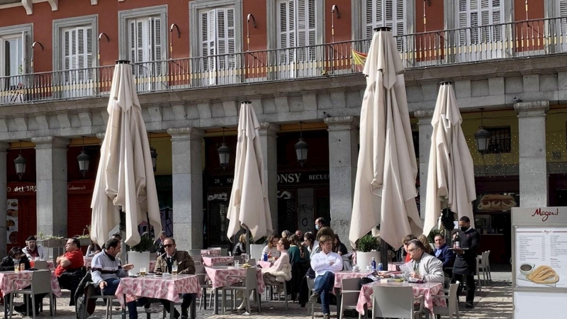 Varios turistas en su mayoría franceses disfrutan del sol en la Plaza Mayor de Madrid.