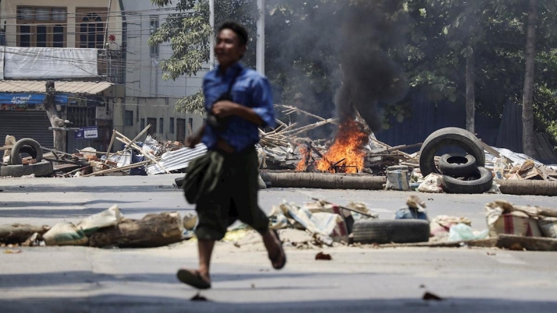 Un hombre corre cerca de una barricada en llamas incendiada por personal militar en un recinto ferroviario en Myanmar