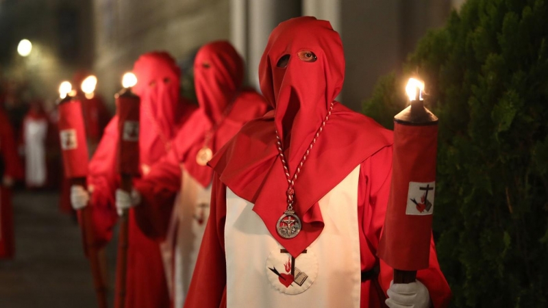 Nazarenos vestidos con túnica blanca y roja y capuz rojo durante una procesión en 2019.