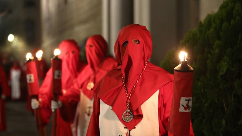 Nazarenos vestidos con túnica blanca y roja y capuz rojo durante una procesión en 2019.