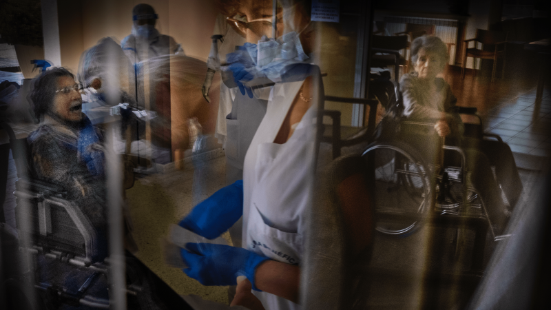 Varias personas mayores reflejadas en un cristal junto a enfermeras que parecen estar vacunando. - Ricardo García Vilanova