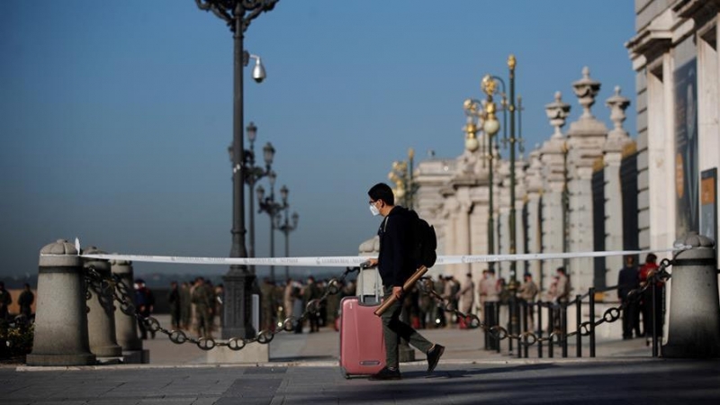 Un joven con su maleta pasa ante el Palacio Real de Madrid.