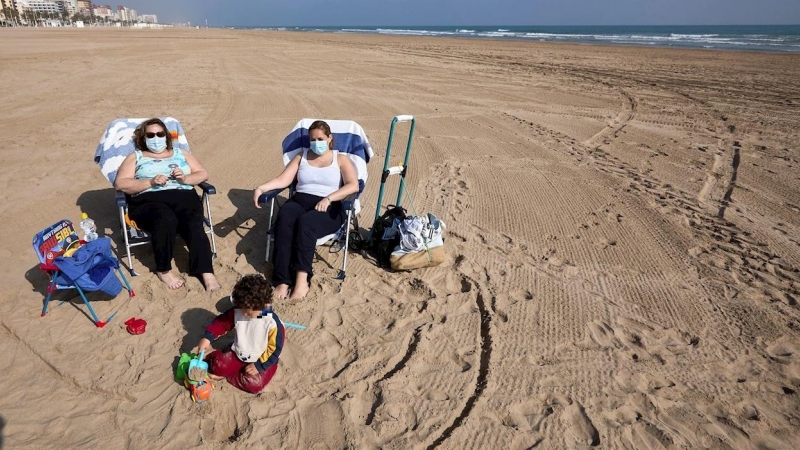 Varias personas toman el sol con mascarilla en la playa de Gandía.