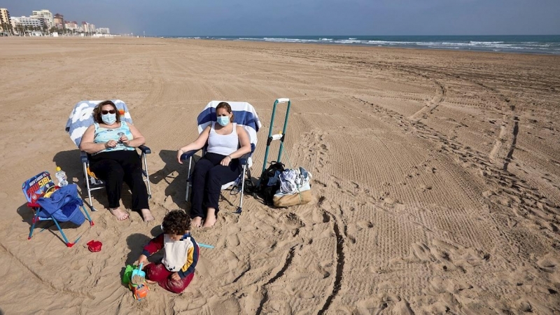 Varias personas toman el sol con mascarilla en la playa de Gandía.