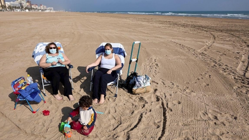 Varias personas toman el sol con mascarilla en la playa de Gandía.