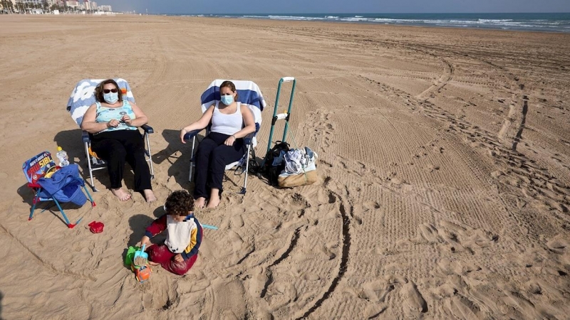 Varias personas toman el sol con mascarilla en la playa de Gandía.