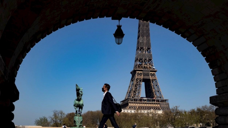 31/03/2021. Un peatón con mascarilla anda por el puente Bir Hakeim cerca de la Torre Eiffel poco antes de que Macron anunciara las nuevas restricciones, este miércoles en París. - EFE