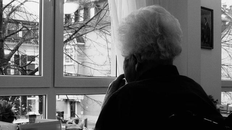 Una persona mayor mira por la ventana de su casa.