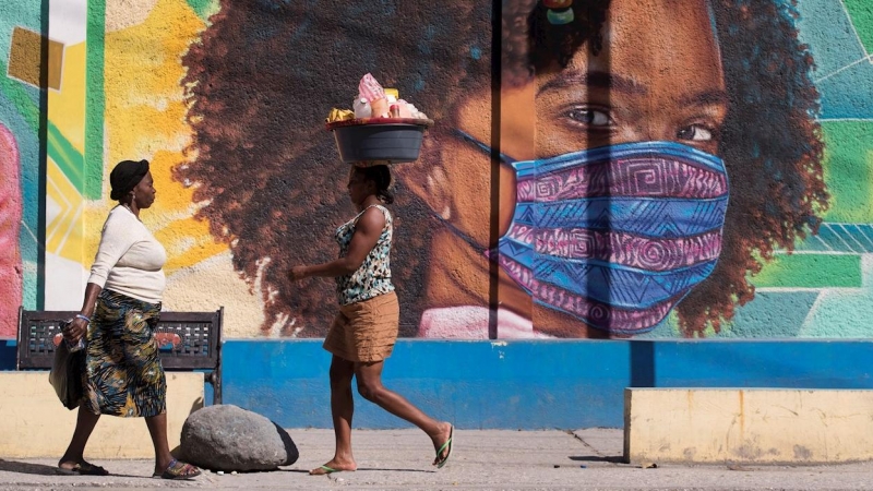 Dos mujeres caminan frente a un mural alusivo al uso del tapabocas por el coronavirus en Puerto Príncipe (Haití).