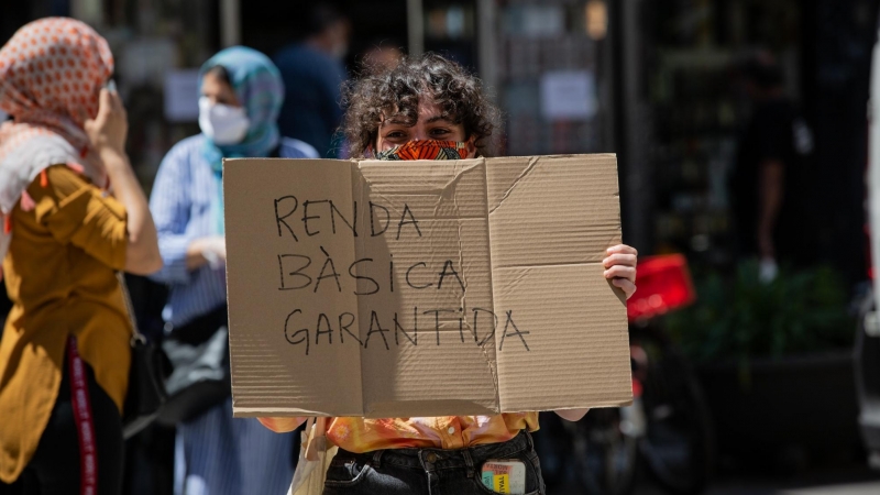 Una dona, acompanyada per membres de la Xarxa veïnal de Suport Mutu Ciutat Vella, agafa una pancarta en la qual es pot llegir 'Renda bàsica garantida'. 22 de maig del 2020.