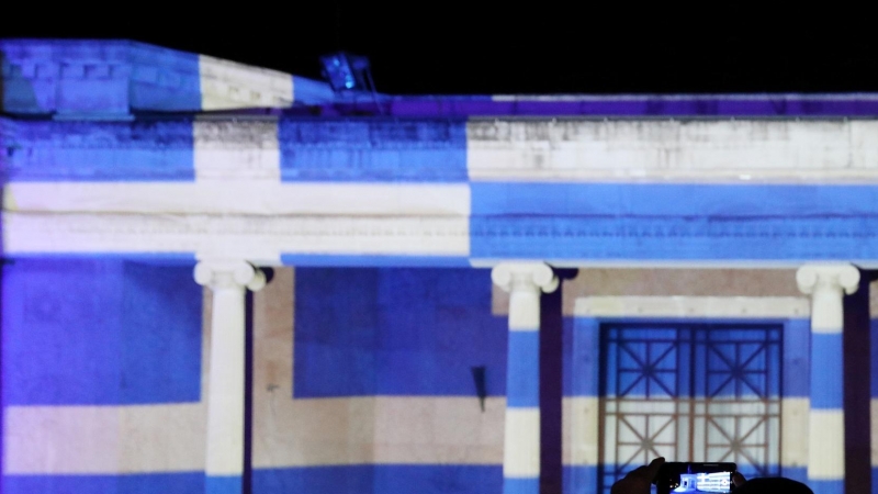 Un hombre toma fotografías frente al antiguo ayuntamiento de Nicosia, iluminado con la bandera griega que marca el 200 aniversario de la Guerra de Independencia de Grecia, en Nicosia, Chipre, el 25 de marzo de 2021.