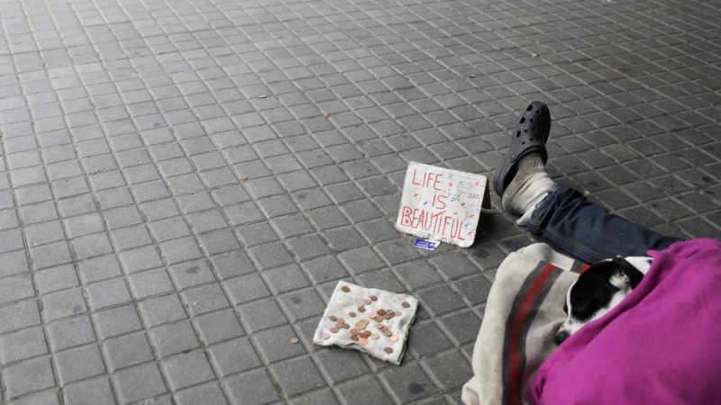 07/04/2020. Imagen recurso de una persona sin hogar en el suelo, junto a unas monedas y un cartel en inglés que dice 'la vida es bella'. - Reuters