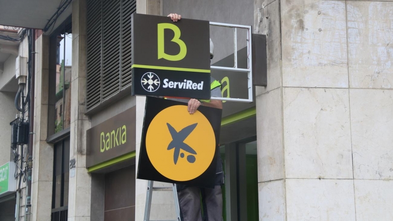 Un operari canviant el logotip de Bankia pel de CaixaBank a l'oficina situada al número 116 de la Rambla del Poblenou de Barcelona. Imatge de 6 d'abril de 2021.