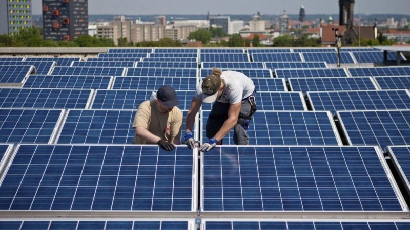 Dos operarios instalan paneles solares en el tejado de un edificios.