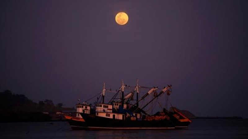 Dos embarcaciones navegan cerca de la costa bajo la Superluna rosa que se eleva en el cielo al principio de la noche hoy, en el pueblo pesquero de Puerto Caimito (Panamá)