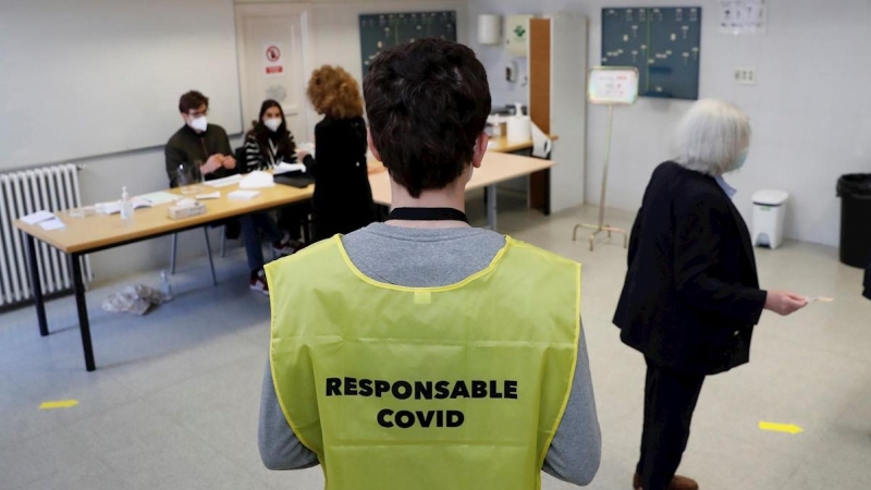 04/05/2021.- Un responsable del cumplimiento de las indicaciones para evitar contagios por covid supervisa la votación de varios ciudadanos en un colegio electoral de Madrid.