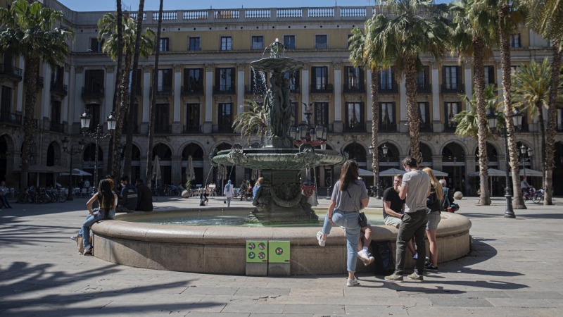 Uns joves descansen i parlen a la font de la plaça Reial