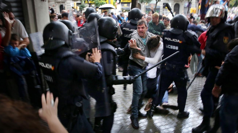 Un home intenta protegir una dona dels cops de porra d'agents antidisturbis de la policia espanyola l'1 d'octubre d'aquest 2017.