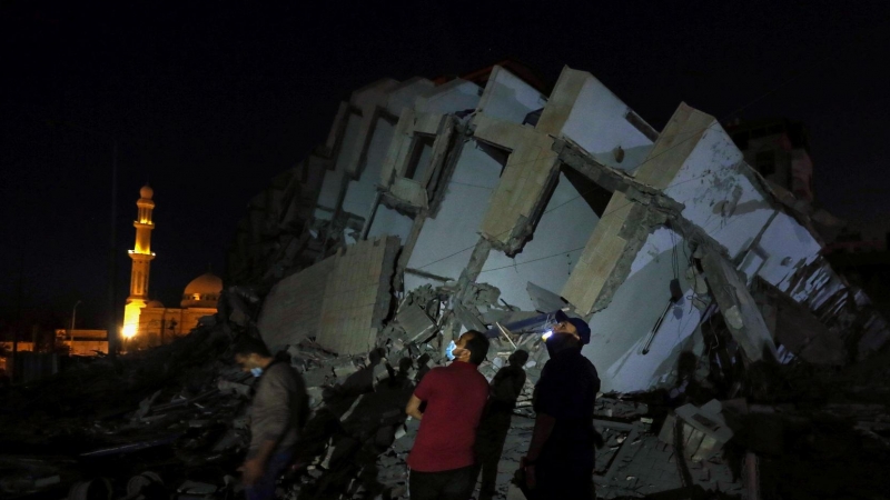 Varios palestinos en el lugar donde un edificio fue destruido por los ataques aéreos israelíes en medio de un estallido de violencia israelí-palestina