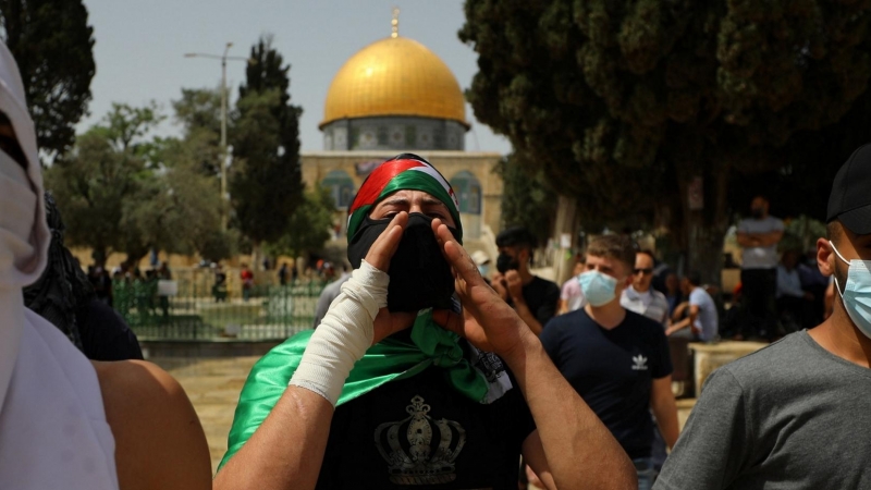 El gesto de palestinos enmascarados cuando la Cúpula de la Roca se ve en el fondo luego de los enfrentamientos con la policía israelí en el complejo que alberga la Mezquita de al-Aqsa, conocida por los musulmanes como el Noble Santuario y por los judíos c
