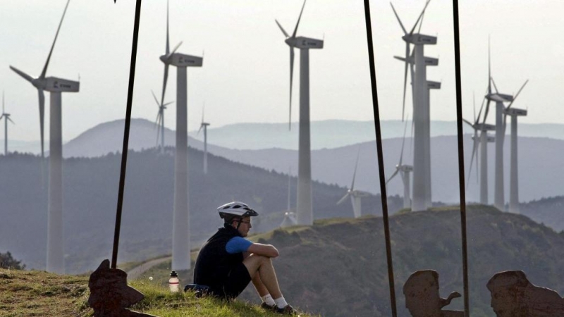 Un ciclista descansa en la Sierra del Perdón, Pamplona, con un paisaje dominado por aerogeneradores eólicos.
