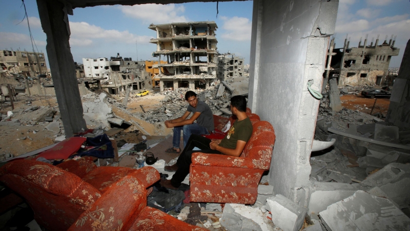 Palestinos sentados en un sofá mientras regresan a los restos de su casa en el este de la ciudad de Gaza